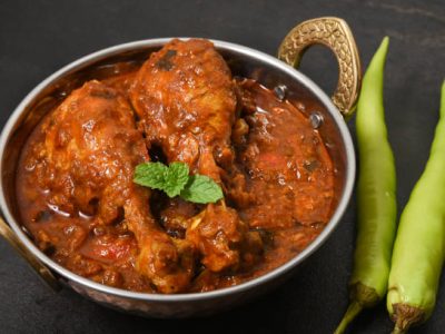 Indian spicy chicken curry top view. Traditional kerala chicken curry two legs cooked in thick gravy with herbs and spices mint leaf. Side dish for appam puttu chapatti parota served in iron or copper bowl with dark black background